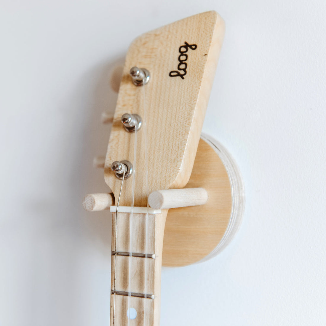 Loog guitar neck secured on a natural birch wood wall mount.