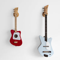 Red and light blue Loog guitars displayed on wooden wall hangers.
