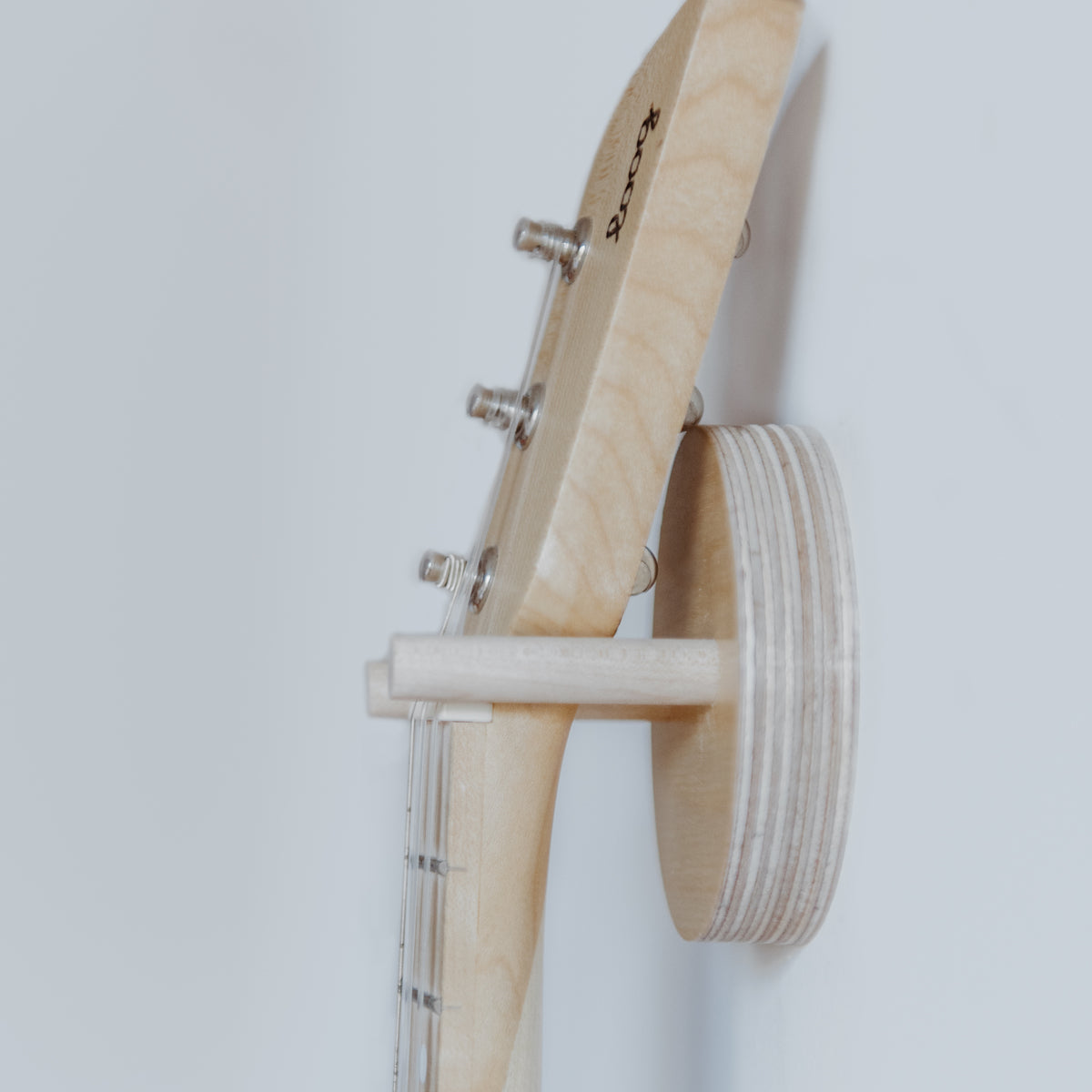 Side view of a Loog guitar on a birch wall hanger.