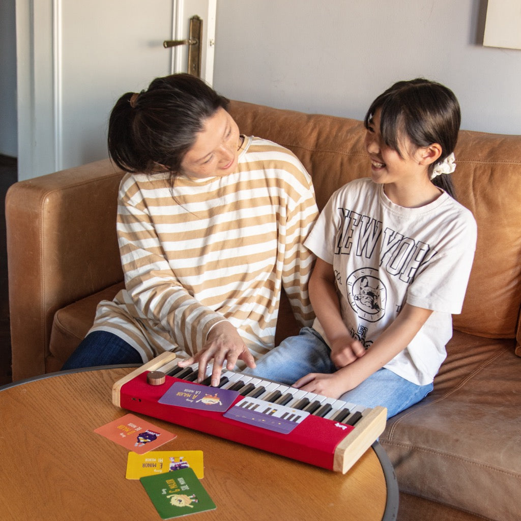Mother and daughter playing red Loog piano on coffee table.