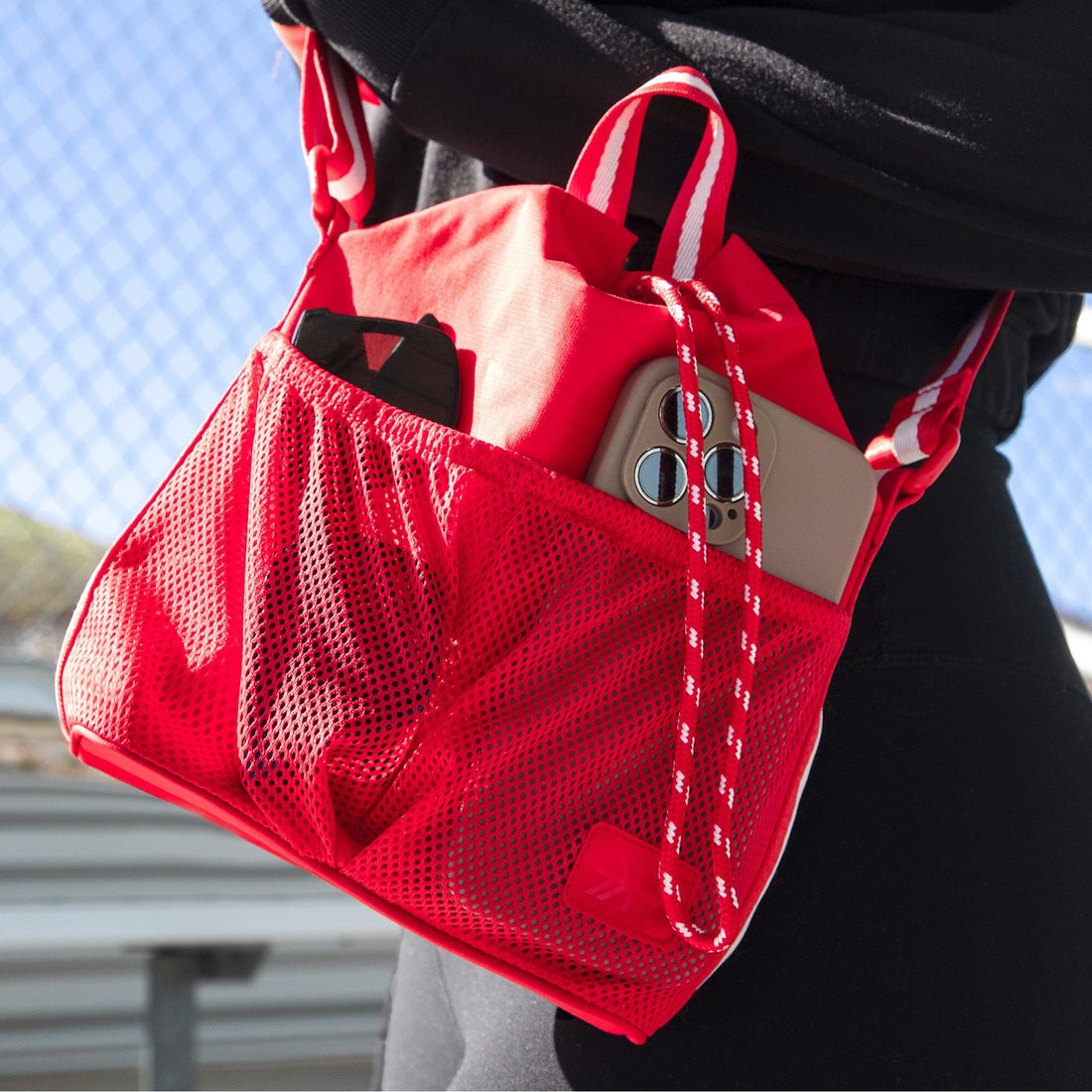 Close-up of the Cherry Motion Bucket Crossbody bag in red, worn over the shoulder, showcasing phone and wallet.