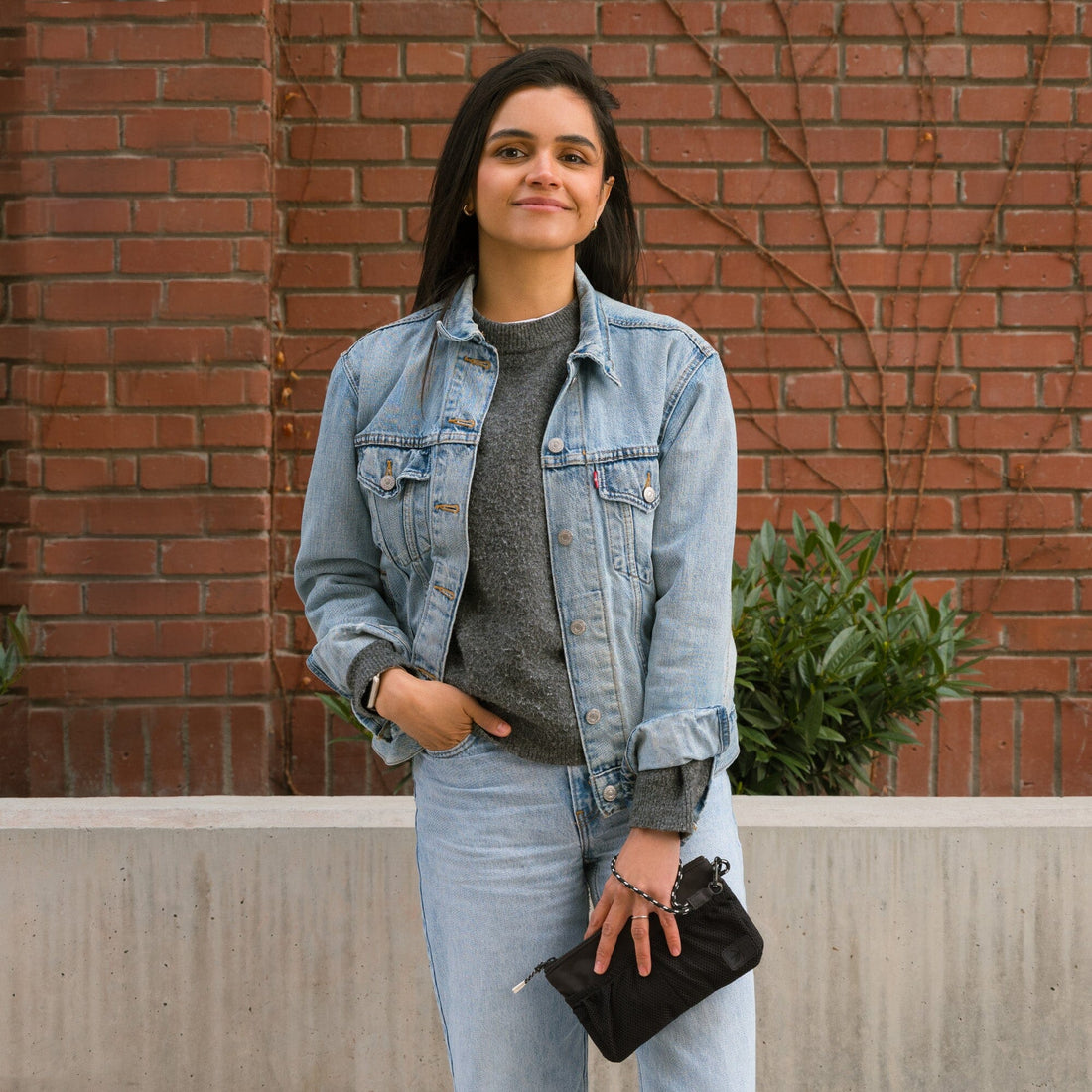 Woman holding a black Jet Motion Wristlet Pouch against a brick wall.