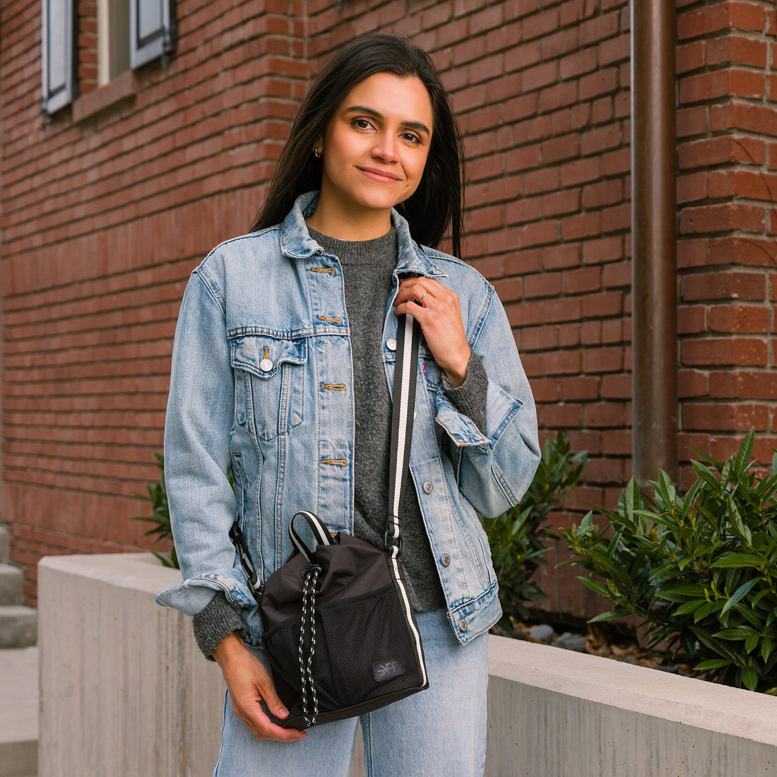 Woman wearing the Jet Motion Bucket Crossbody bag in black with a denim jacket.