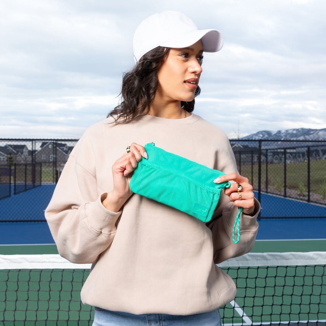 Woman holding Kelly Motion Wristlet Pouch in green at a tennis court.