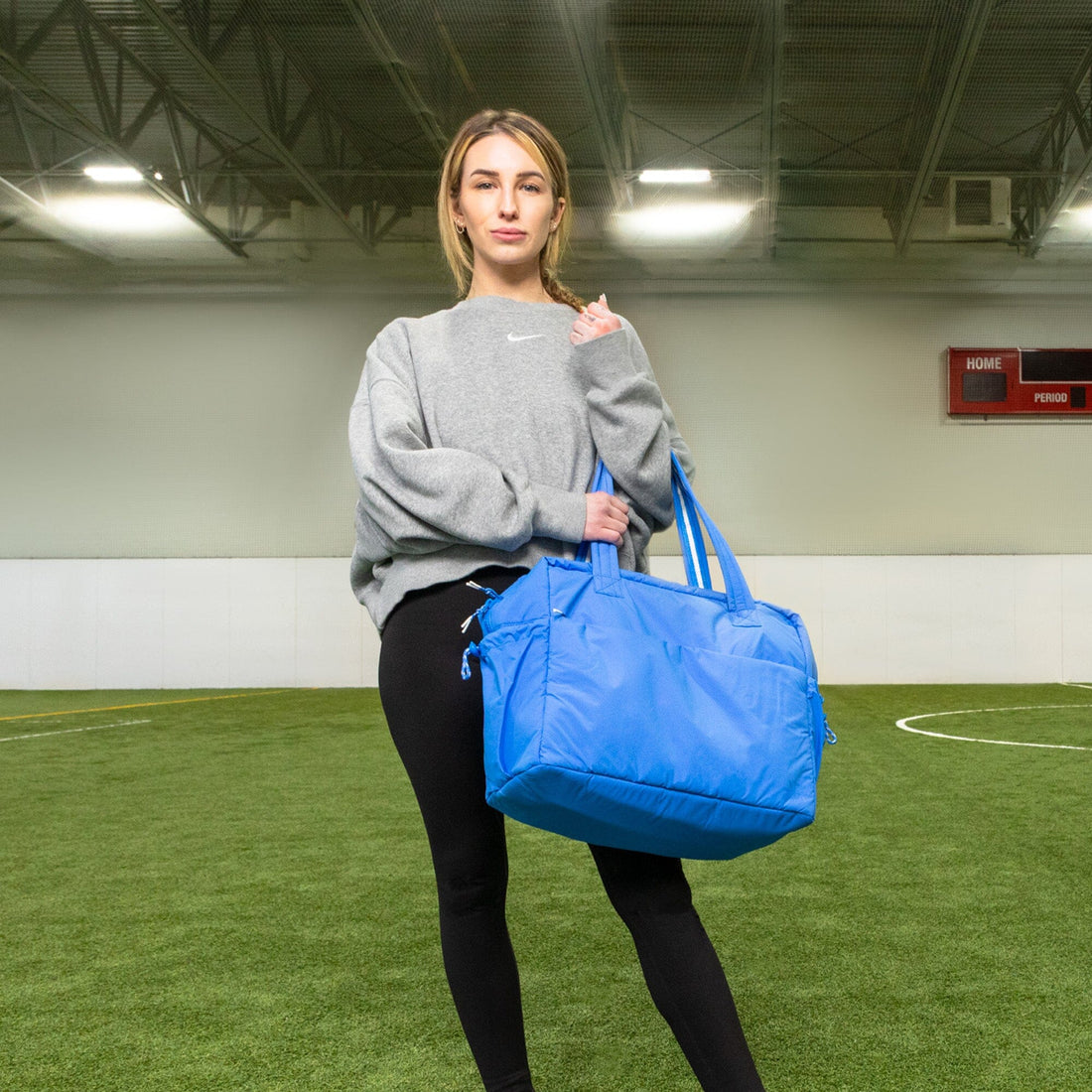 Woman holding a blue Wave Motion Overnight Duffle bag in a gym.