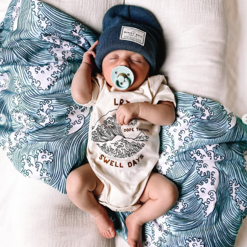 Baby in cream Dope Threads Swell Days organic cotton onesie with wave graphic.
