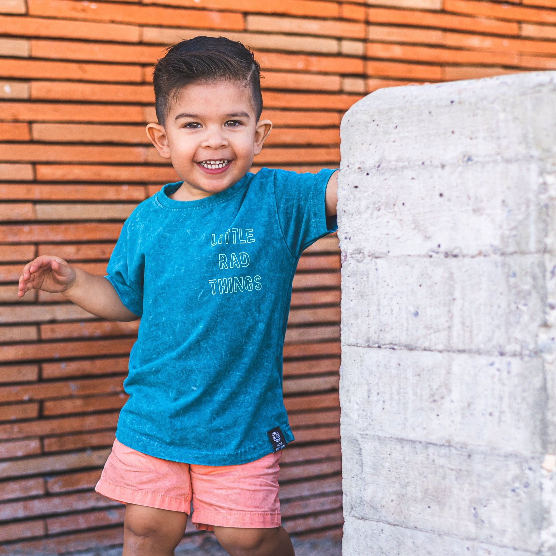 Smiling boy in 'Little Rad Things' tee and peach shorts