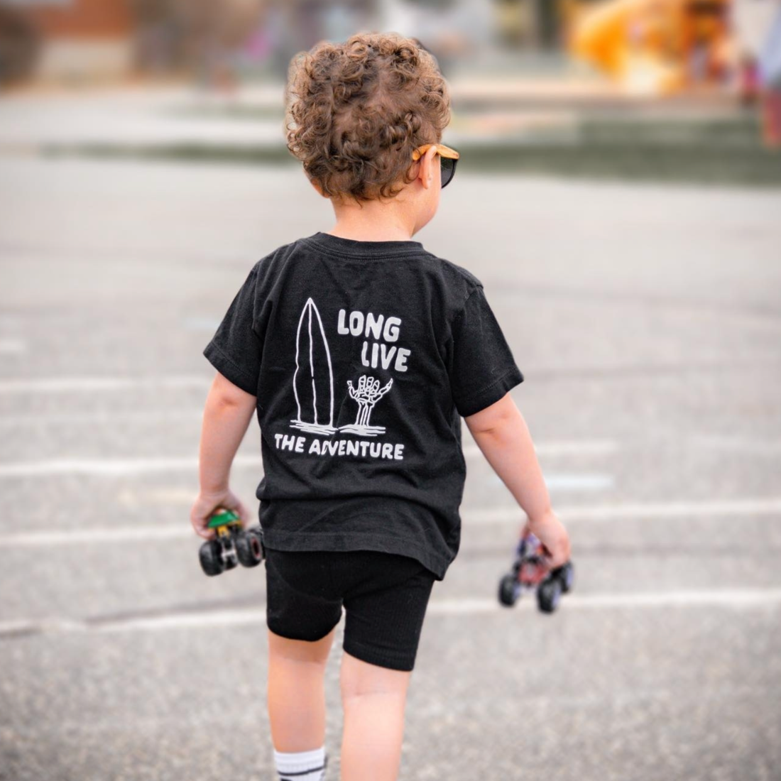 Child wearing Long Live The Adventure black tee with toy cars.