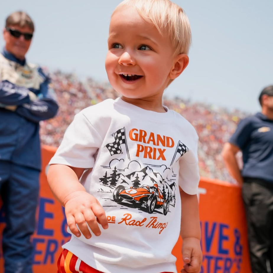 Smiling child wearing a Grand Prix t-shirt at a racetrack event.