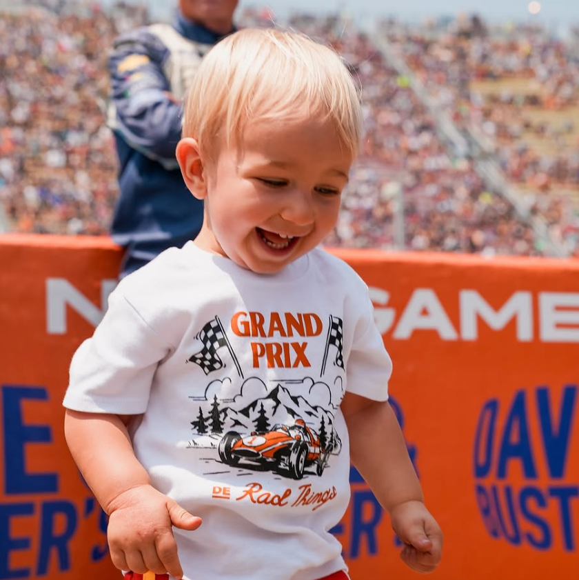 Toddler smiles wearing the white Grand Prix de Rad Things tee.