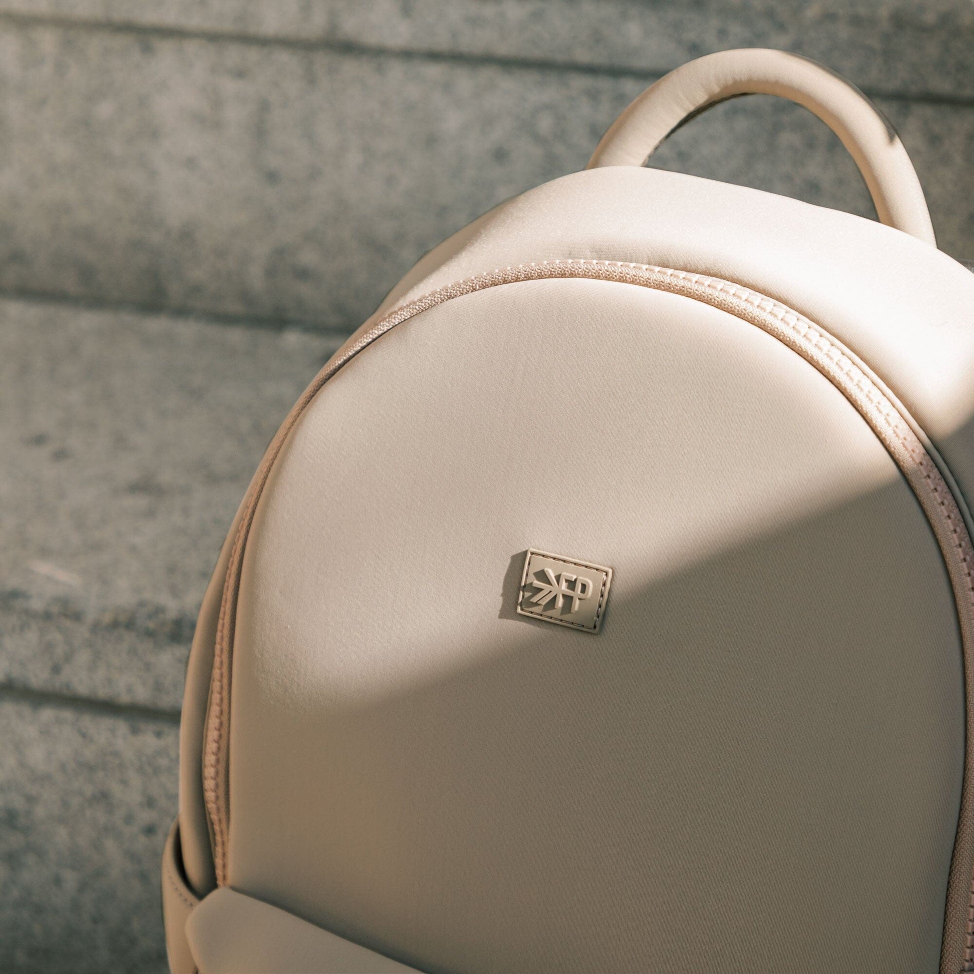 Close-up of the Aspen Seoul Backpack in Sand color and logo.