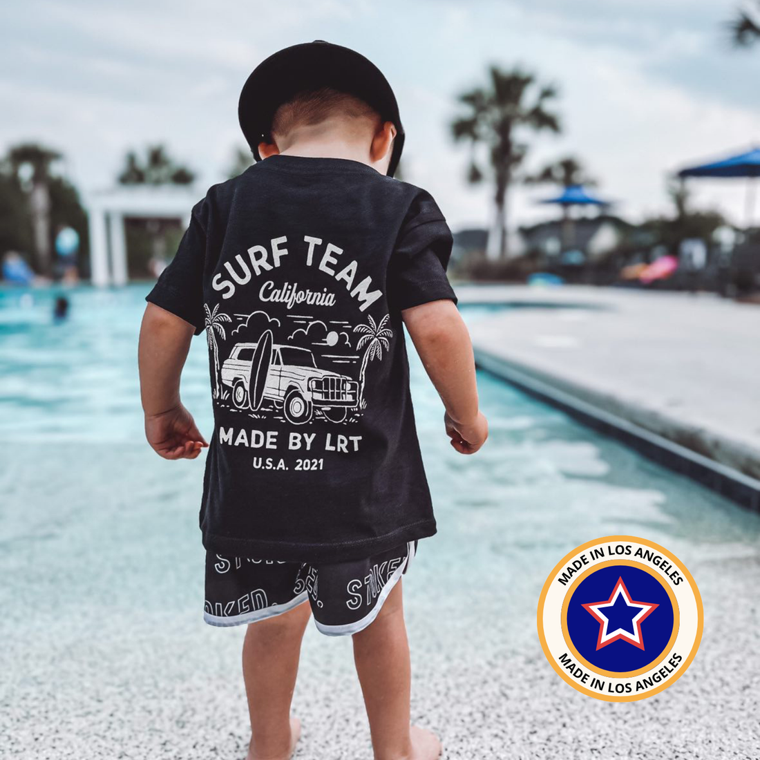 Toddler wearing black Surf Team tee with white graphic, standing near pool.