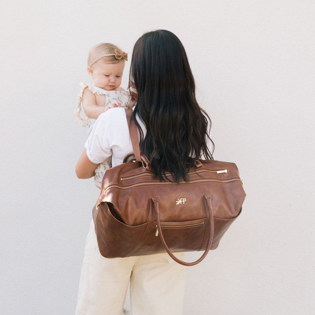 Amber Minimal Weekender bag worn over the shoulder, holding a baby.