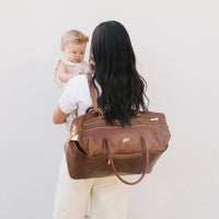 Amber Minimal Weekender bag worn over the shoulder, holding a baby.
