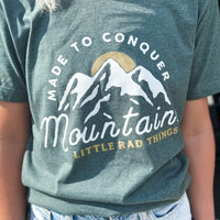 Close-up of the 'Made To Conquer Mountains' graphic on a green tee.