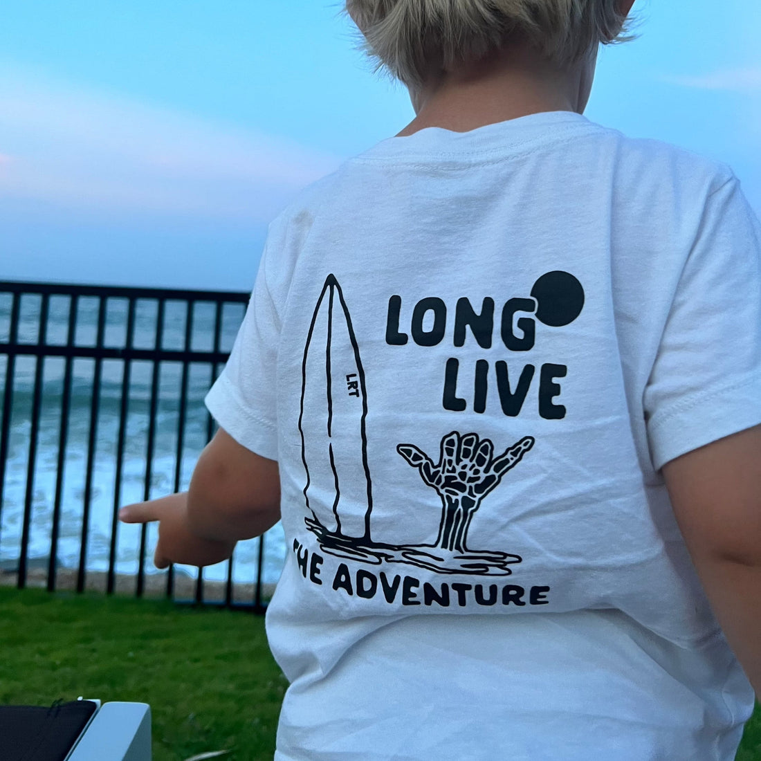 Child wearing Long Live The Adventure Tee in white by the ocean.