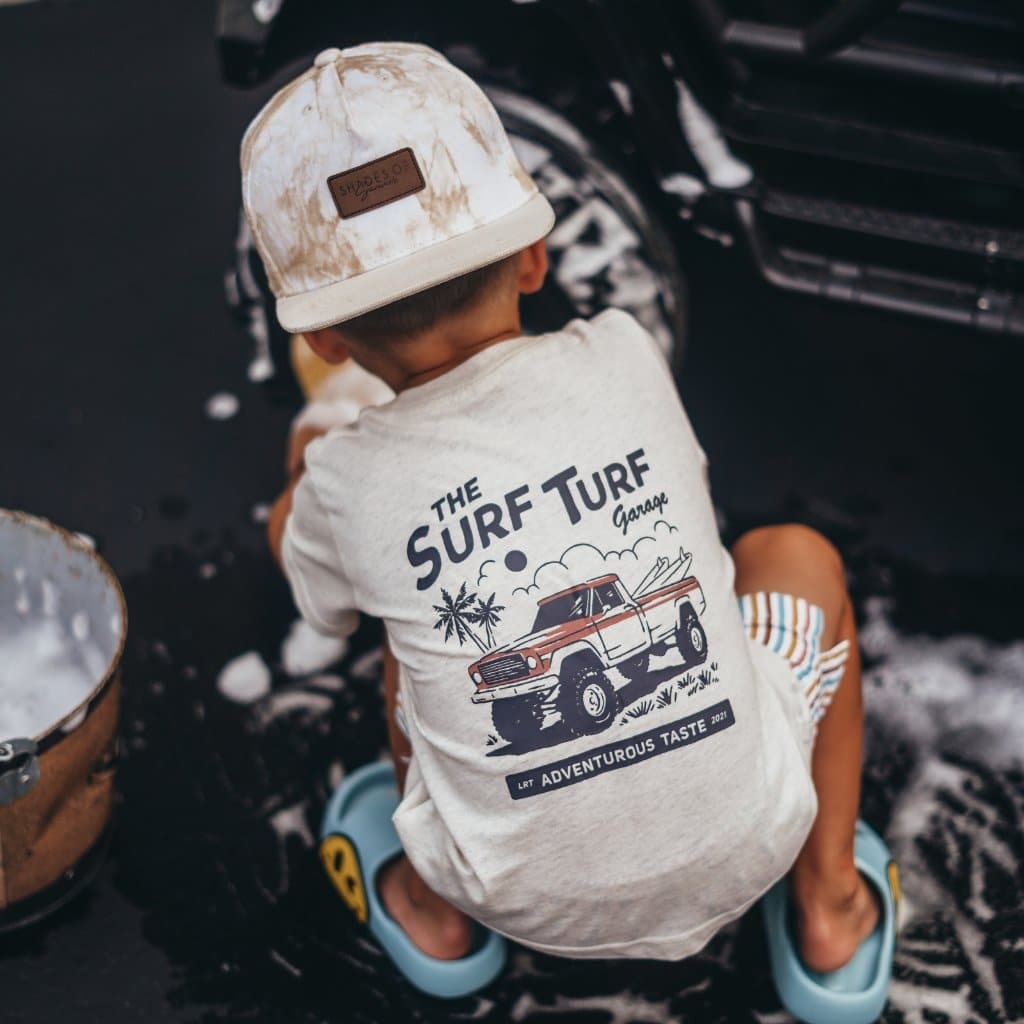 Boy washing toy car in Surf Turf Tee with truck graphic and ball cap