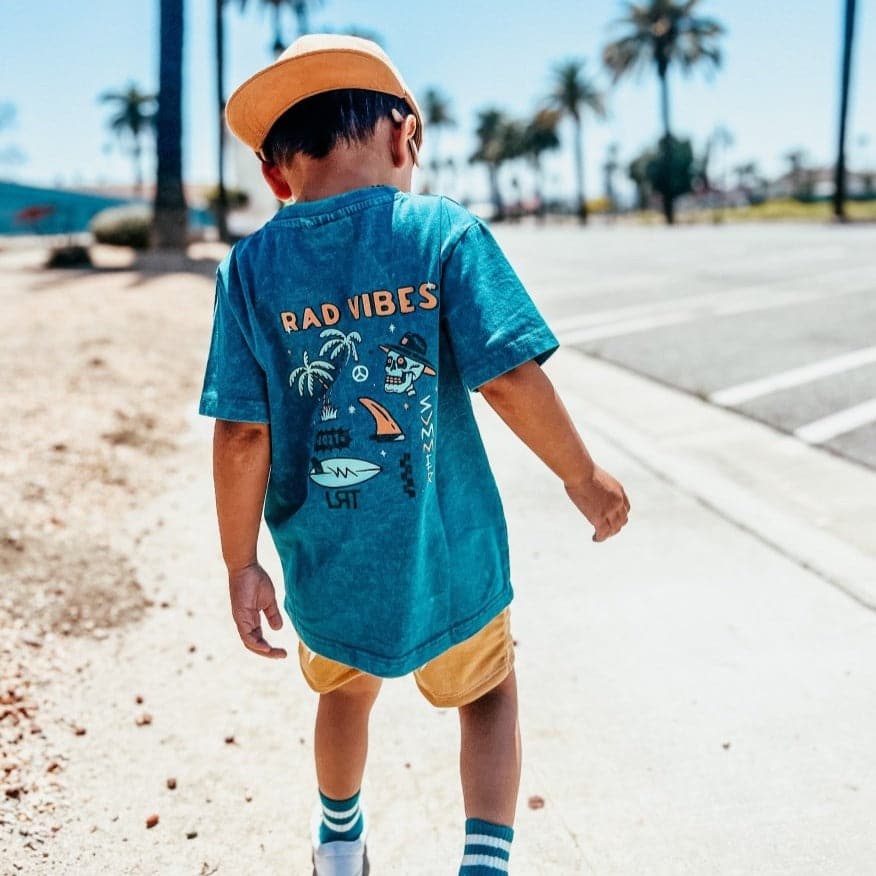 Child in 'Rad Vibes' tee and gold shorts walking outdoors